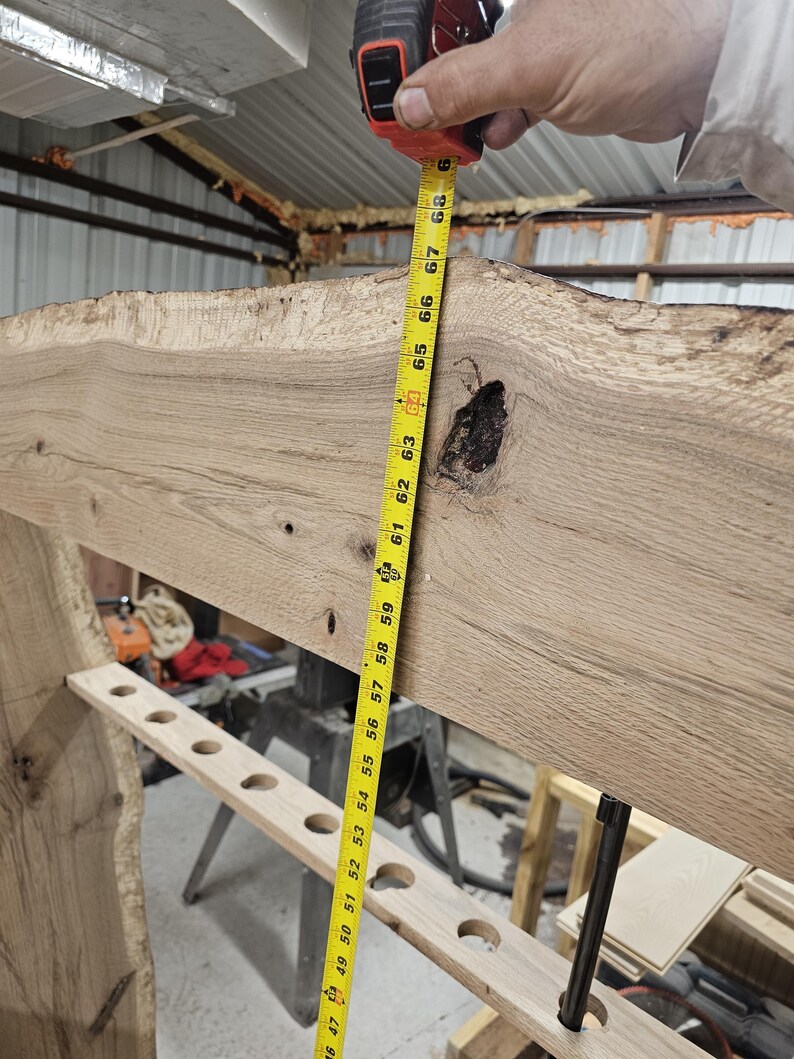 K&ouml;nnte beinhalten: Ein helles, unfertiges Holzbalken mit einer rohen Kante, gemessen mit einem gelben Ma&szlig;band. Das Ma&szlig;band zeigt eine L&auml;nge von etwa 173 cm. Der Balken hat einen Knoten und mehrere L&ouml;cher.