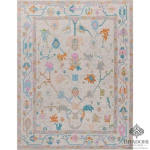 May include: A rectangular area rug with a cream-colored background and a detailed floral pattern in shades of blue, orange, pink, and gray. The rug has a border with a repeating floral design. The rug is a traditional style.