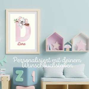 Könnte beinhalten: Gerahmter Druck mit einem Aquarell-Koala auf einem Ast über einem rosa Buchstaben "D". Der Name "Dora" steht in roter Schrift darunter. Der Hintergrund ist cremefarben.