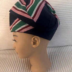 May include: A navy blue hat with a striped pattern in green, pink, and white. The hat is displayed on a mannequin head. The hat's design features a folded construction, showcasing the colorful stripes prominently. The hat is a fashion accessory.