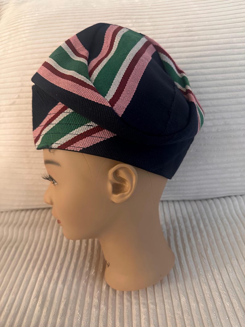 May include: A navy blue hat with a striped pattern in green, pink, and white. The hat is displayed on a mannequin head. The hat's design features a folded construction, showcasing the colorful stripes prominently. The hat is a fashion accessory.