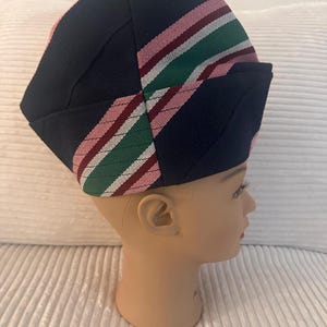 May include: A navy blue hat with a striped pattern in pink, green, and white. The hat is placed on a mannequin head. The hat's design features a folded brim and a structured crown, showcasing a blend of colors and textures.