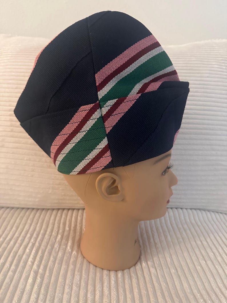 May include: A navy blue hat with a striped pattern in pink, green, and white. The hat is placed on a mannequin head. The hat's design features a folded brim and a structured crown, showcasing a blend of colors and textures.