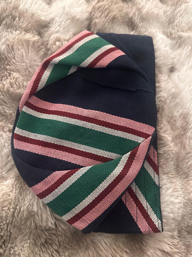 May include: A navy blue hat with a striped band in green, white, and pink. The hat is folded over, showcasing the contrasting colors and textures of the fabric. The stripes are evenly spaced.
