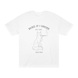 May include: White t-shirt featuring a black illustration of a fox smoking. The text above reads "MIND IF I SMOKE EST. 1985", with "JAVA TREE" below. The shirt is a relaxed fit, suitable for everyday wear.