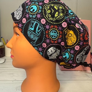 May include: Black surgical scrub cap with a colorful pattern of skulls, floral designs, and Star Wars-themed characters. The cap features a variety of colors including blue, yellow, pink, and white. The cap is designed to be worn in a medical setting.