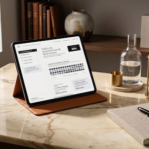May include: A tablet with a brown leather case displays a webpage with the text "Indice de Arquitectura de Momentum". A notebook, pen, hourglass, and water bottle sit on a marble surface. A small gold cup and a decorative box are also visible.
