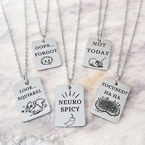 May include: Silver-toned necklaces with rectangular pendants. Each pendant has a different engraved design and text: "OOPS... FORGOT", "NOT TODAY", "LOOK... SQUIRREL", "NEURO SPICY", and "FOCUSED? HA HA".