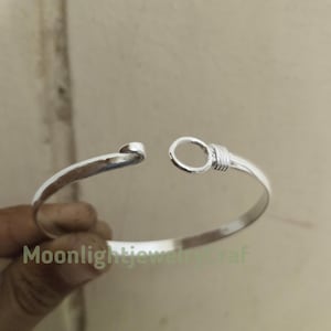 May include: A silver-colored cuff bracelet with an open design. The bracelet has a smooth, polished finish and features a loop and hook closure. The text "Moonlightjewelcraft" is visible on the bracelet.