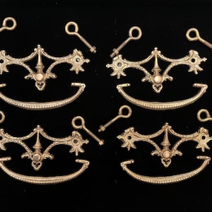 May include: A collection of antique brass furniture hardware, including ornate drawer pulls, decorative backplates, and keyhole escutcheons. The hardware has a detailed, vintage design, perfect for restoration projects. The pieces are arranged on a black background.