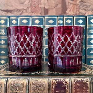 May include: Two matching ruby red glass tumblers featuring a clear cut diamond pattern on the upper half and vertical fluted panels along the base. The glasses have a thick, weighted bottom and a smooth, straight-sided cylindrical shape.