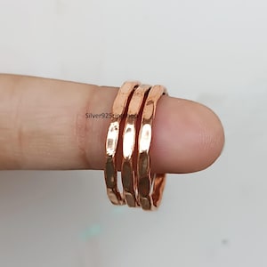 May include: Three copper-colored rings with a hammered, textured finish. Each ring features a reflective, metallic surface with irregular indentations. The text Silver925ringshop is visible on the surface of the middle ring in the set.
