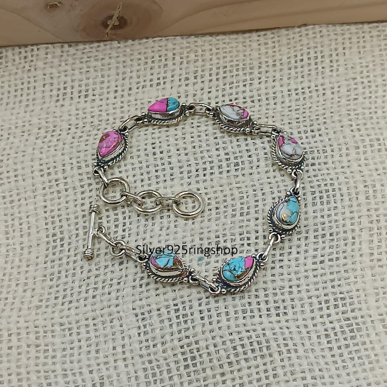 May include: A silver bracelet featuring teardrop-shaped stones in shades of pink, turquoise, and white. The stones are set in a silver frame and connected by a chain. The bracelet has a toggle clasp. The text "Silver925ringshop" is visible.