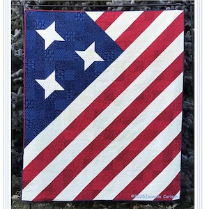 May include: A patriotic quilt featuring the American flag design. The quilt has a blue corner with white stars and red and white stripes. The text "United We Stand" is at the top. Finished size is 64" x 76".