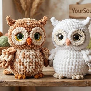 May include: Two handmade crochet owl plushies, one brown and one white, sit side-by-side on a wooden surface. The owls have large, expressive eyes and are surrounded by yarn, crochet hooks, and a sign that reads "YourSoulDesigner."