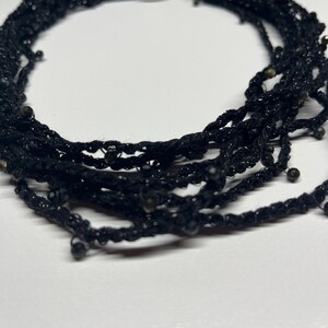 May include: Black multi-strand necklace with small beads. The necklace is made of a woven material and has a silver clasp. The necklace is a choker style and is suitable for formal or casual wear.