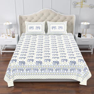 Op de afbeelding: Witte beddengoedset met een herhalend patroon van blauwe olifanten en bloemaccenten. Inclusief twee kussenslopen met olifantenontwerpen. Het beddengoed heeft een decoratieve rand met een blauw en goud patroon.