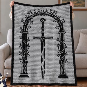 May include: A rectangular crochet blanket featuring a light gray background with a black border. The design displays a central black sword positioned beneath a tall, arched stone-like gateway entwined with climbing vines, all rendered in black.