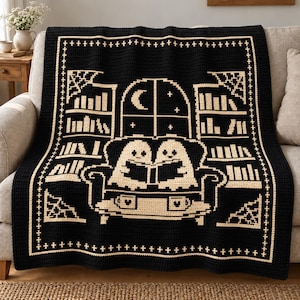 May include: A black and cream crochet blanket featuring a central design of two ghosts sitting on a sofa reading books, flanked by bookshelves, a window with a crescent moon, and a border pattern of small crosses and corner spider web motifs.