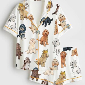 May include: White pajama set featuring a repeating pattern of various dog breeds, each adorned with crowns, bow ties, and party hats. The short-sleeved top and shorts have orange trim.