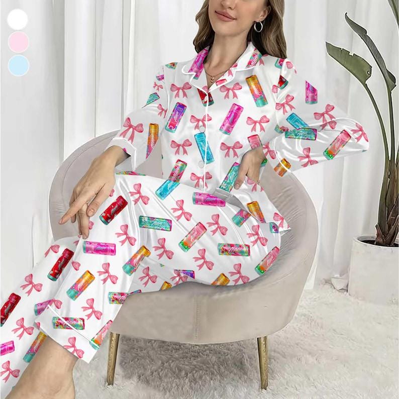 May include: White satin pajama set with a lipstick and pink bow pattern. The long-sleeved top and pants feature a button-down shirt design with white piping. The lipstick designs are in various colors.