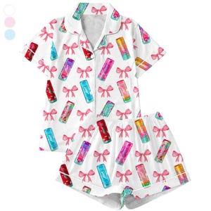 May include: White pajama set with a pattern of colorful beverage cans and pink bows. The short-sleeved top has a collared neckline and button-up front. The matching shorts have a drawstring waist.