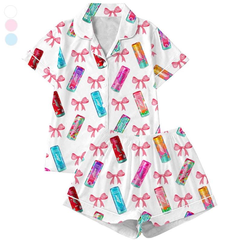 May include: White pajama set with a pattern of colorful beverage cans and pink bows. The short-sleeved top has a collared neckline and button-up front. The matching shorts have a drawstring waist.