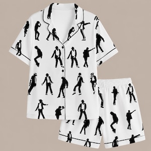 Puede incluir: Conjunto de pijama blanco con ribete negro, con un patrón repetido de figuras de silueta negra en varias poses de baile. El conjunto incluye una camisa con botones de manga corta y pantalones cortos a juego.