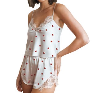 May include: White satin pajama set with red heart embroidery. The camisole top features a lace trim along the neckline. The matching shorts also have lace trim along the hemline. A comfortable and stylish sleepwear set.