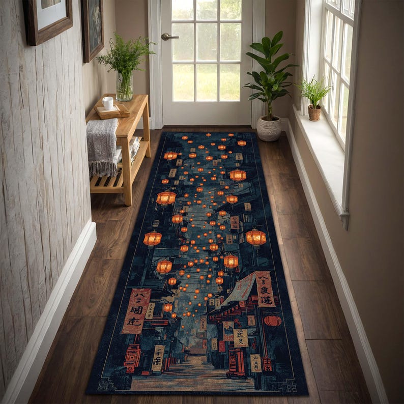 Puede incluir: Una alfombra larga y rectangular con una ilustraci&oacute;n detallada de una escena callejera nocturna. La alfombra presenta un fondo azul oscuro con faroles y edificios naranjas. El dise&ntilde;o evoca una calle de una ciudad asi&aacute;tica.