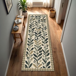 Può includere: Un tappeto runner rettangolare con un design botanico. Il tappeto presenta uno sfondo color crema con file verticali di foglie e bacche verde scuro e verde oliva. Il bordo ha un motivo ripetuto. Il tappeto è posato su un pavimento in legno.