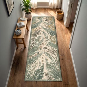 Puede incluir: Una alfombra de pasillo rectangular larga con un patrón botánico de hojas de helecho verdes y marrones sobre un fondo color crema. La alfombra tiene un borde fino y está colocada en el centro de un suelo de madera en un pasillo.