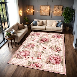 May include: A large rectangular area rug with a floral pattern. The rug features large pink peony flowers, cherries, and green leaves on a light pink and white checkered background. The rug is placed in a living room with beige sofas.