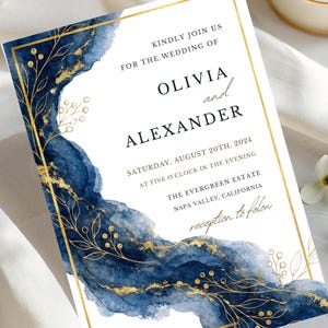 Può includere: Invito di nozze con sfondo bianco, accenti acquerello blu navy e dettagli dorati. L'invito include i nomi Olivia e Alexander, la data, l'ora e il luogo del matrimonio.