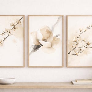 May include: Three framed watercolour prints with floral designs in soft beige and brown tones. The prints depict delicate branches with flowers and a large magnolia bloom. The frames are light brown, and the overall aesthetic is serene and natural.