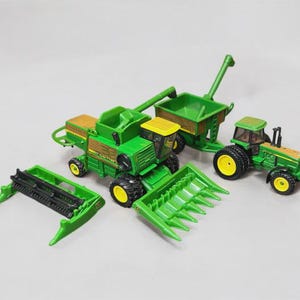 Puede incluir: Un conjunto de vehículos agrícolas de juguete verdes y amarillos, que incluyen una cosechadora, un tractor y un carro de grano. La cosechadora tiene un cabezal desmontable. El tractor tiene neumáticos negros con llantas amarillas.