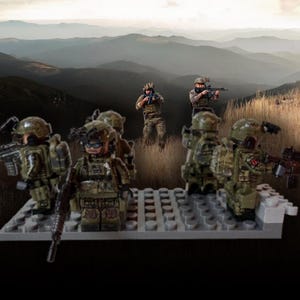 Op de afbeelding: Een groep miniatuur militaire figuren in camouflage-uniformen, helmen en tactische uitrusting, met geweren. Ze staan op een grijze basis, tegen een achtergrond van glooiende heuvels en een bewolkte lucht. De scène roept een gevoel van actie en strategie op.