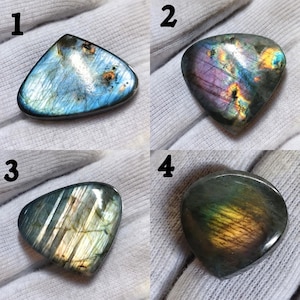 Può includere: Quattro pietre preziose di labradorite lucidata, ognuna con variazioni di colore uniche. La gemma 1 è blu e grigia. La gemma 2 è viola e oro. La gemma 3 è verde e oro. La gemma 4 è verde e oro.