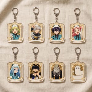 以下が含まれることがあります： 装飾的な金色の枠で囲まれたアニメスタイルのキャラクターイラストが描かれた、8つの長方形のアクリルキーホルダーセット。各キーホルダーには銀色の金属製ロブスタークラスプと、下部に空白の白いバナーが付いています。