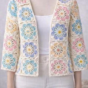 May include: Cream crochet jacket with a floral pattern in pastel shades. The jacket has a V-neck and three-quarter sleeves. The floral design includes light blue, pink, and yellow, creating a soft, feminine appearance.