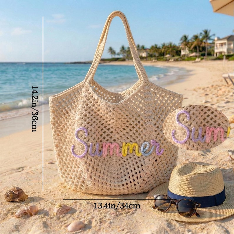 K&ouml;nnte beinhalten: Beige H&auml;keltasche mit dem Wort "Summer" in Pastellfarben. Die Tasche ist 36 cm hoch und 34 cm breit. Ein Strohhut mit marineblauem Band und Sonnenbrille liegen neben der Tasche am Strand.