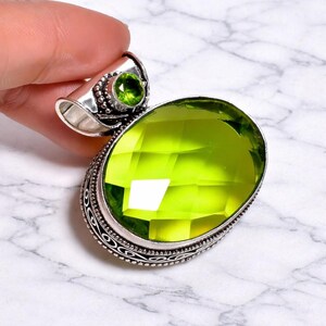May include: A silver pendant featuring a large, oval-cut, lime-green gemstone. A smaller, round, green stone is set above the larger stone. The pendant has an ornate, detailed silver setting.