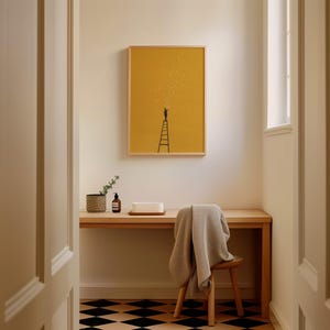 May include: A framed art print featuring a person on a ladder reaching for stars against a mustard yellow background. The artwork is displayed above a wooden desk with a chair and a patterned floor.