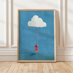May include: A framed art print featuring a child in a red dress swinging from a cloud against a blue sky. The artwork has a whimsical, illustrative style, with a light wooden frame.