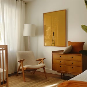 May include: A cozy bedroom scene featuring a wooden crib, a mid-century modern chair, and a wooden dresser. A framed yellow artwork with a person on a ladder is mounted on the wall. The room is illuminated by natural light and a floor lamp.