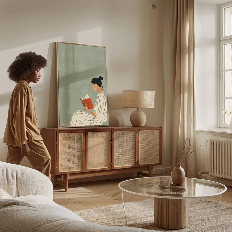 Pu&ograve; includere: Scena di soggiorno con un mobile in legno con pannelli intrecciati, una stampa artistica incorniciata di una persona che legge, un tavolo rotondo e una lampada beige. Una persona in abito marrone cammina vicino al mobile.