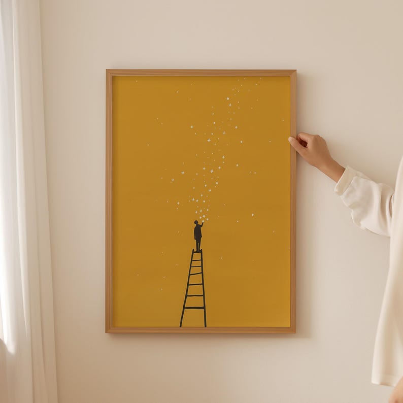 May include: A framed art print featuring a minimalist illustration. A black silhouette of a person stands atop a ladder, reaching towards a cluster of white stars against a mustard yellow background. The frame is made of light brown wood.