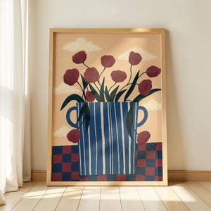 May include: A framed wall art print featuring a blue and white striped vase with two handles, filled with dark red flowers and green leaves. The background is a light peach color with white clouds, set above a red and blue checkered surface.