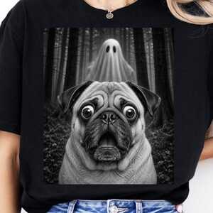 Może przedstawiać: Czarny t-shirt z nadrukiem graficznym przedstawiającym mopsa z szeroko otwartymi oczami i otwartym pyskiem, umieszczonego w ciemnym lesie z białą postacią ducha unoszącą się w tle. Projekt jest wykonany w monochromatycznym stylu czarno-białym.