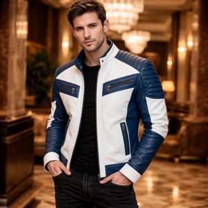 Puede incluir: Chaqueta de cuero de dos tonos en blanco y azul marino. La chaqueta presenta un cuello alzado, bolsillos con cremallera y paneles acolchados en los hombros. La chaqueta se lleva sobre una camisa negra.